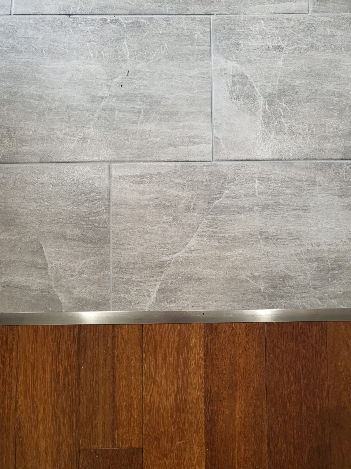 A transition strip separates a section of gray tile flooring from a section of brown wood flooring.