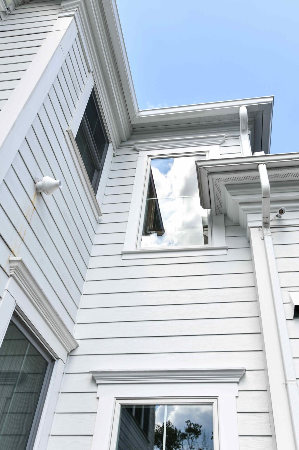 A close-up view of the exterior of a white house with horizontal siding, multiple windows, and visible gutters against a blue sky.