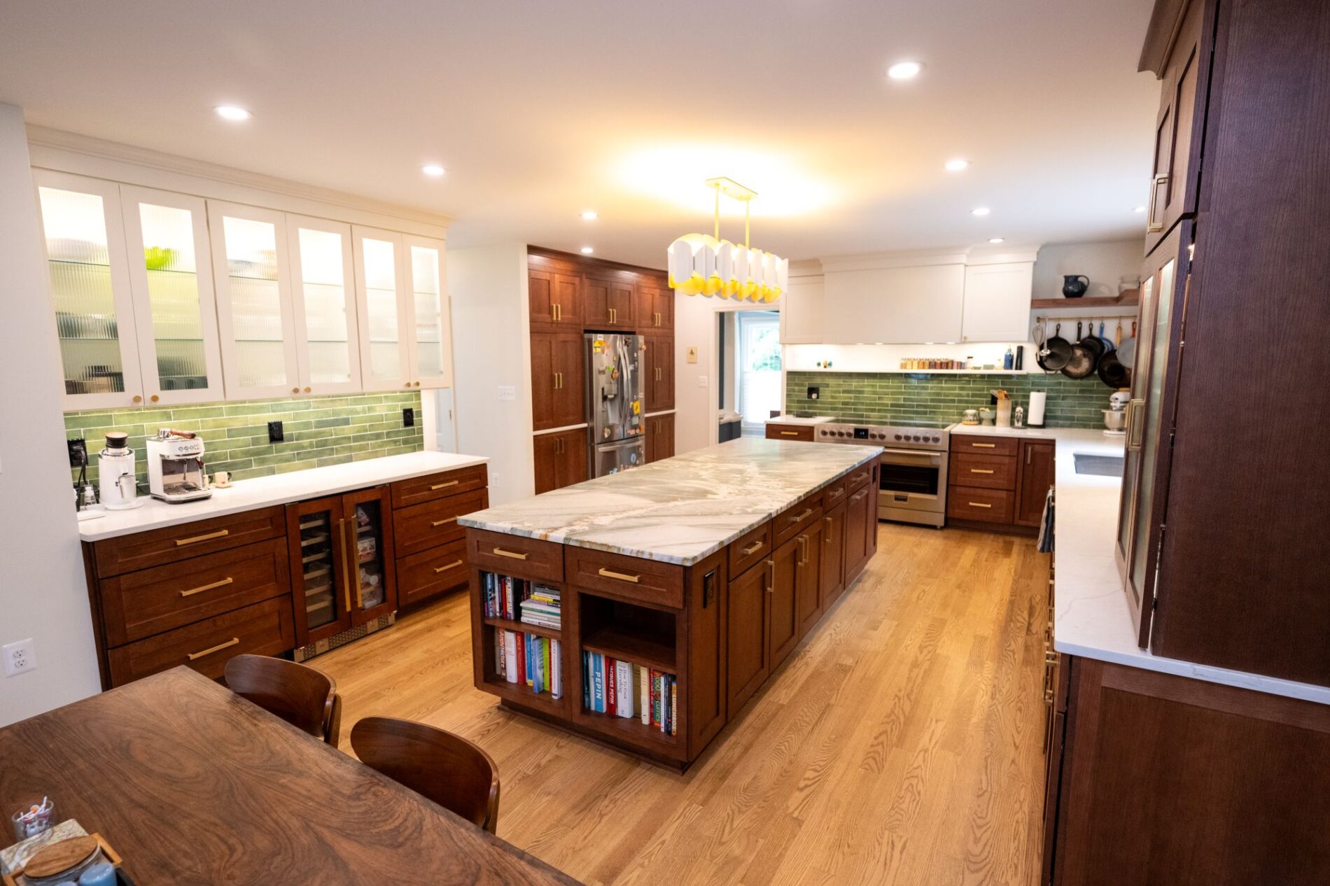 Spacious kitchen with wooden cabinets, marble island with bookshelves, green tile backsplash, modern appliances, and wooden dining table with chairs.