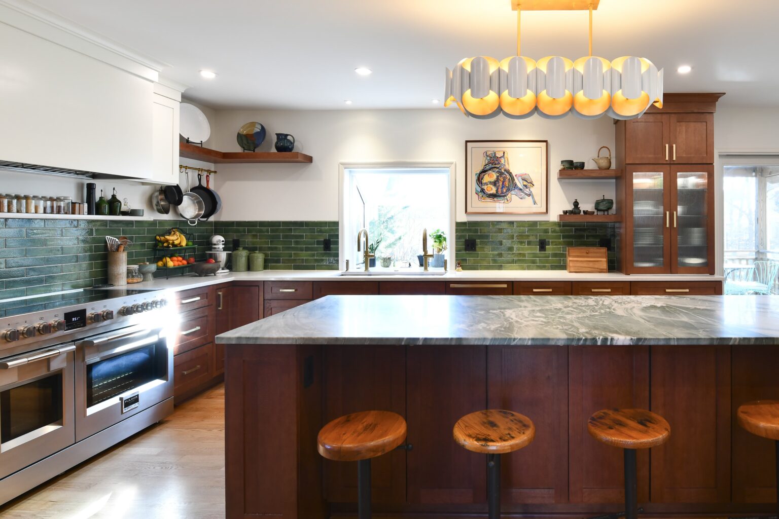 Spacious kitchen with a marble island, wooden stools, stainless steel appliances, green tile backsplash, and modern lighting fixture.