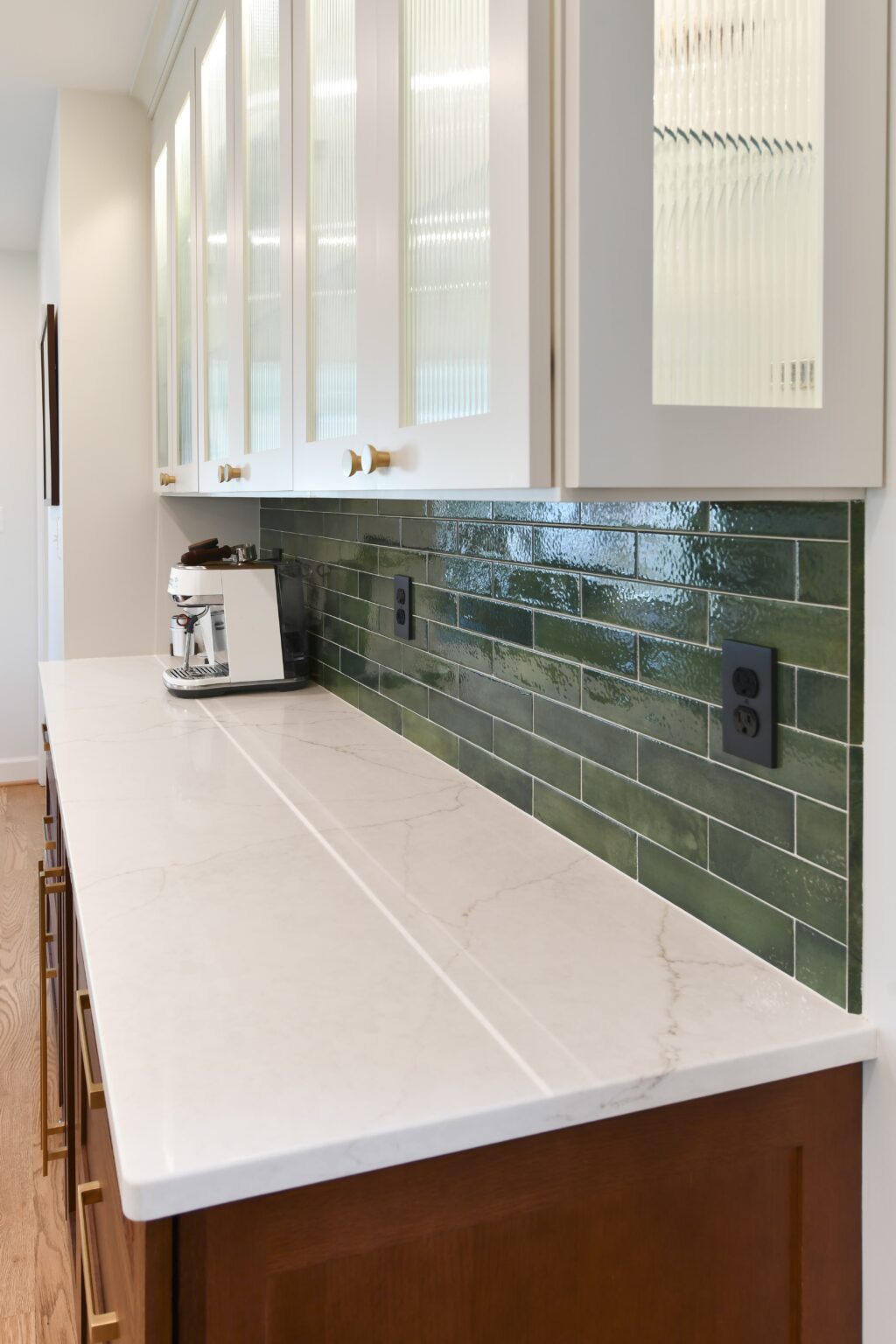 Marble countertop with brown cabinets, white upper cabinets, green subway tile backsplash, and a coffee maker on the counter.