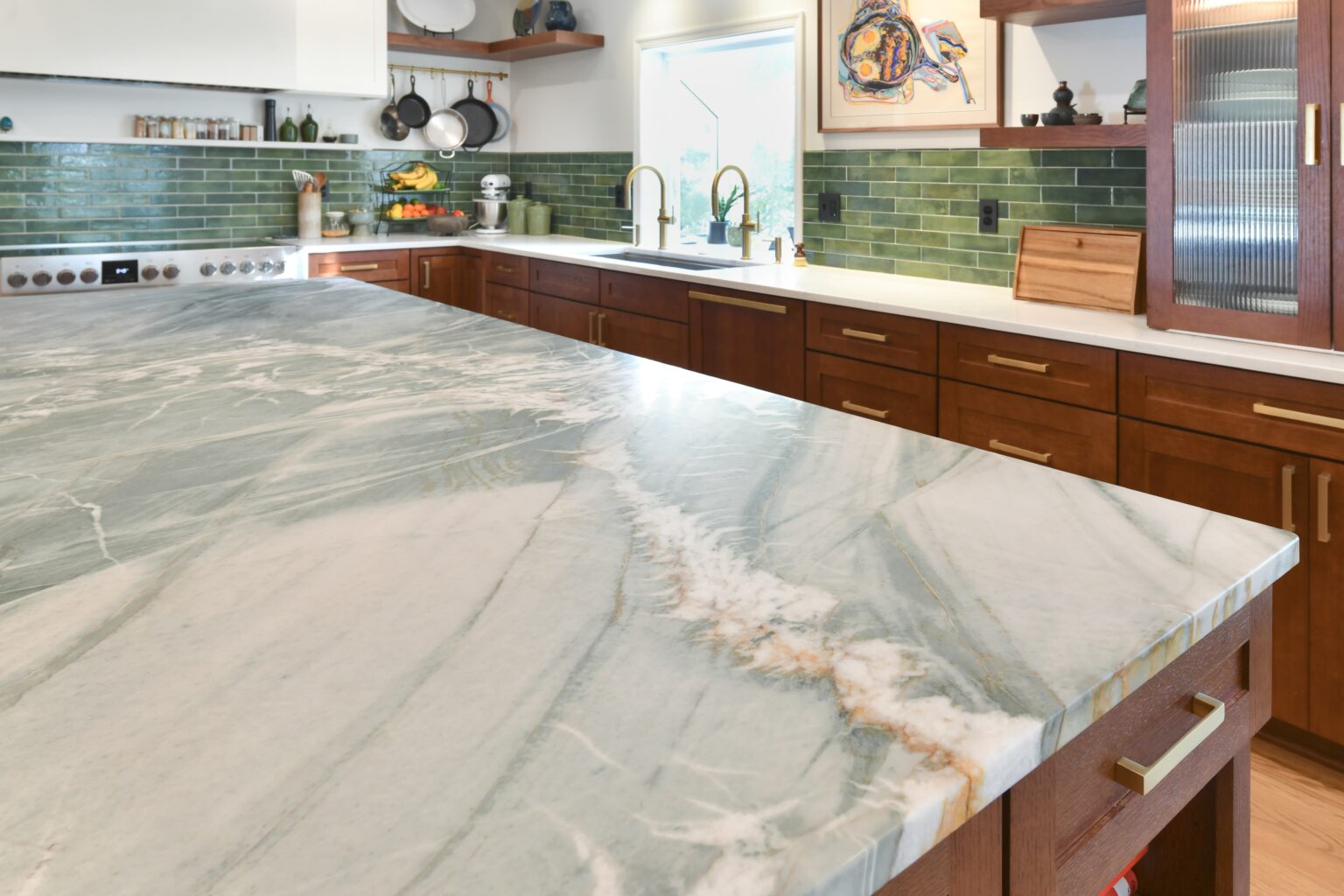 Modern kitchen with a large marble countertop, dark wooden cabinets, green tile backsplash, and open shelving with dishes and plants.