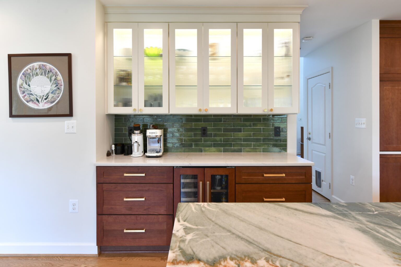 Modern kitchen with dark lower cabinets, glass-front upper cabinets, green tile backsplash, coffee maker, and marble countertop.