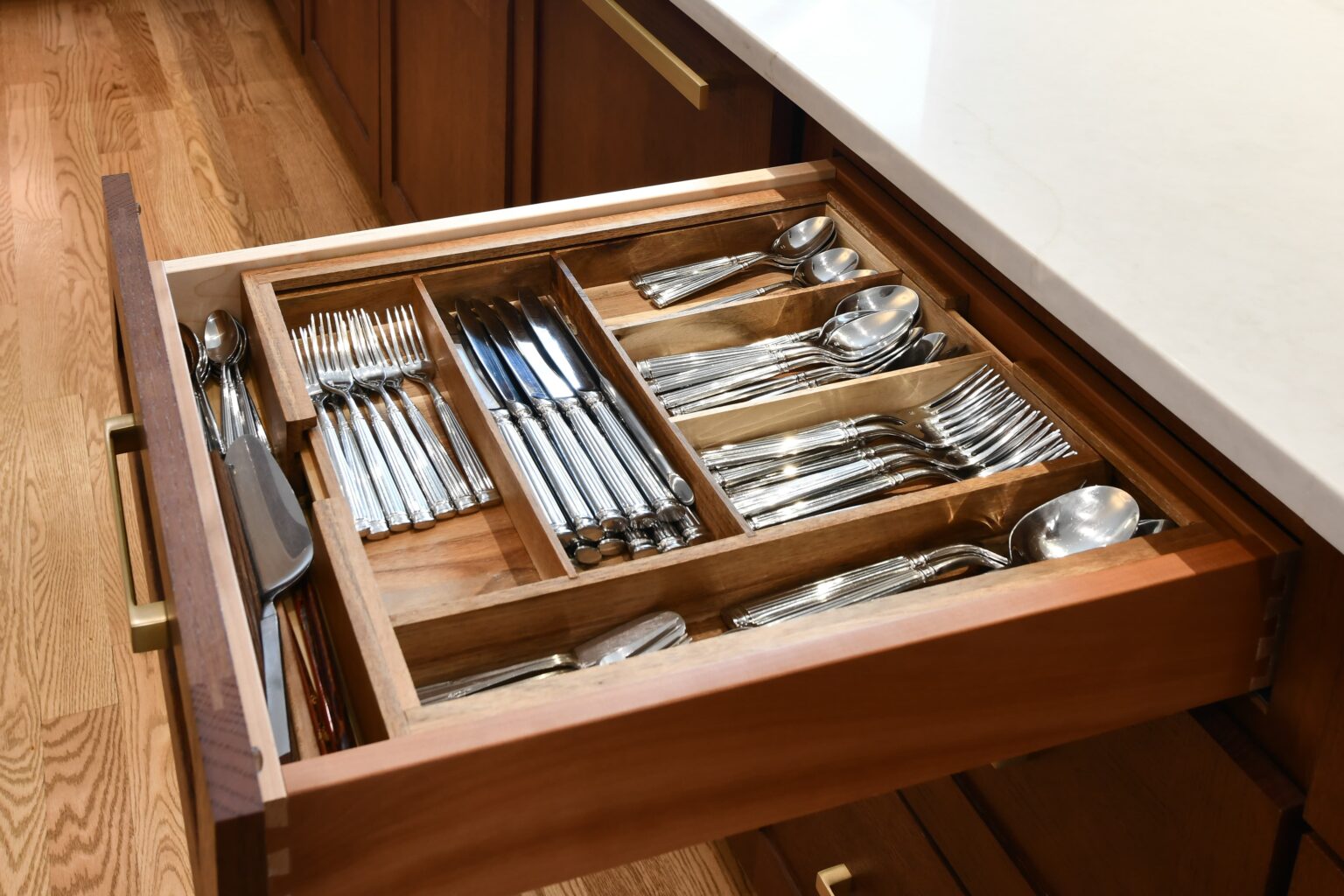 An open kitchen drawer shows organized silverware, including forks, knives, and spoons, neatly arranged in a wooden utensil tray.