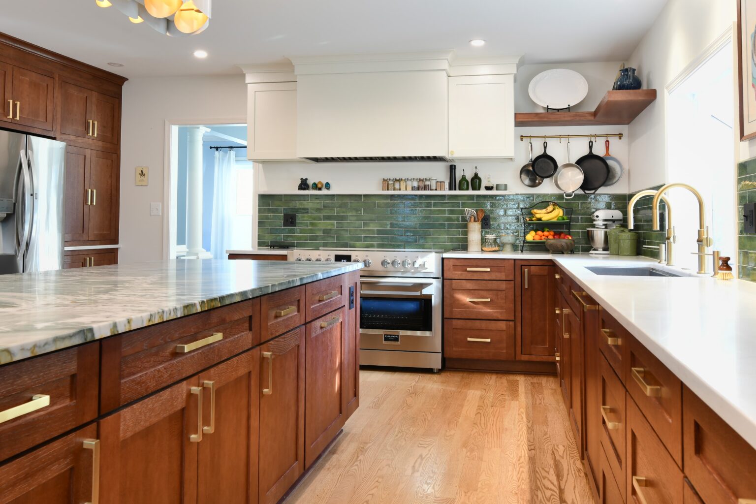 Modern kitchen with wooden cabinets, green tile backsplash, stainless steel appliances, marble island, and open shelves displaying dishes and cookware.