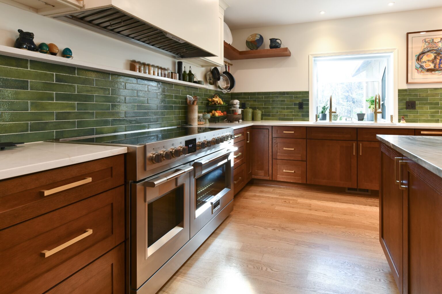Modern kitchen with brown cabinets, stainless steel oven and stove, green tile backsplash, wood floor, and natural light from a window.