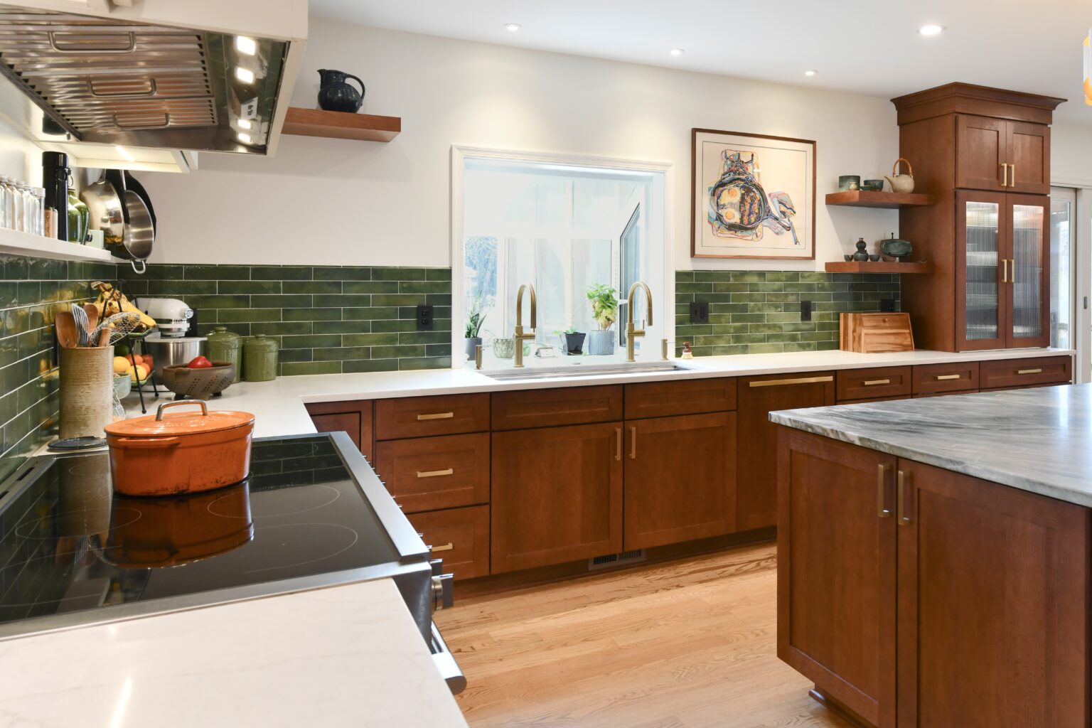 Modern kitchen with wood cabinets, green tile backsplash, double sink under window, and various kitchenware on counters and shelves.