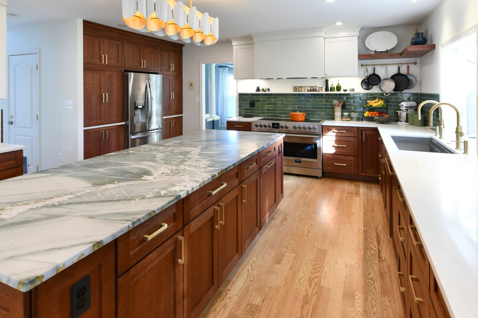 Modern kitchen with wood cabinets, marble island countertop, stainless steel appliances, green tile backsplash, and bright natural lighting.