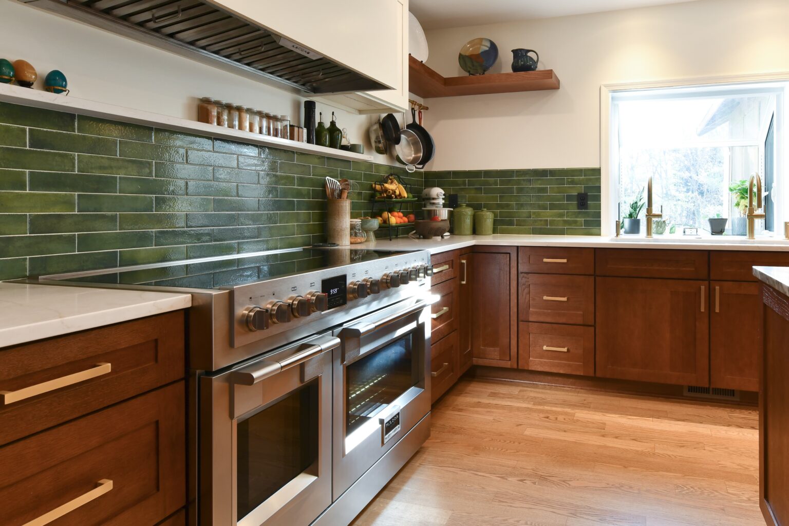 Modern kitchen with green tile backsplash, stainless steel stove, wooden cabinets, open shelves, and sunlight streaming through a window.