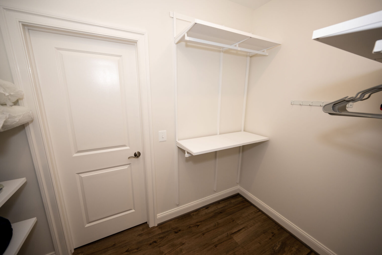 Empty walk-in closet with white walls, shelves, a hanging rod, and a closed white door, featuring wood-style flooring.