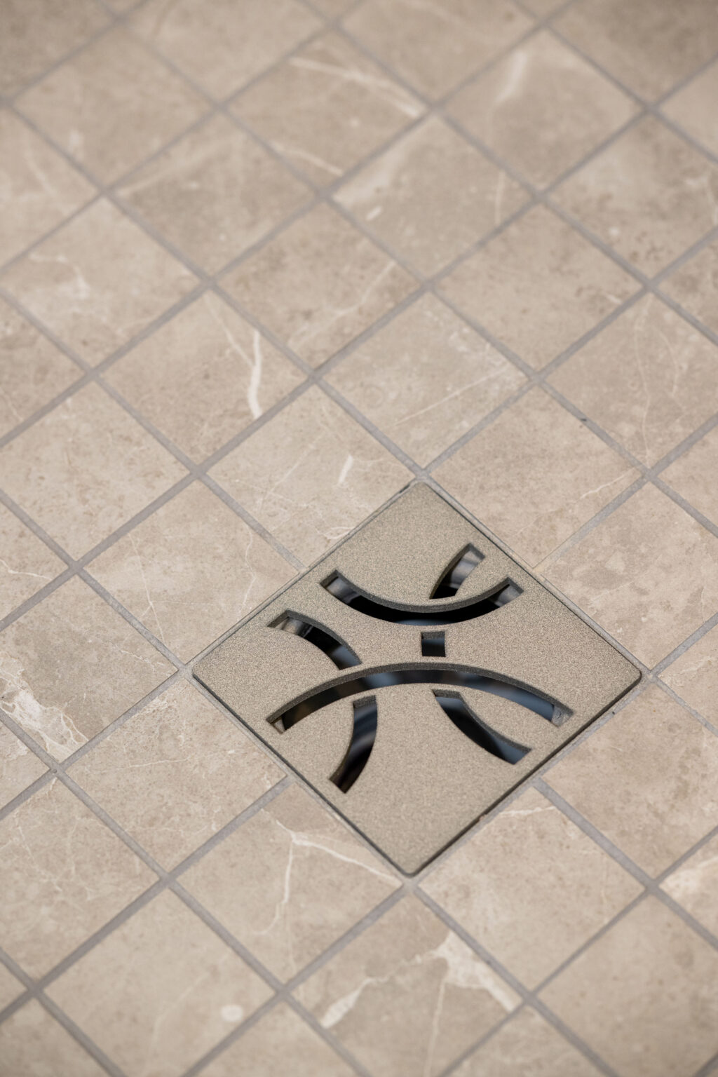 Square tile floor with a central metal drain cover featuring a geometric cutout pattern.
