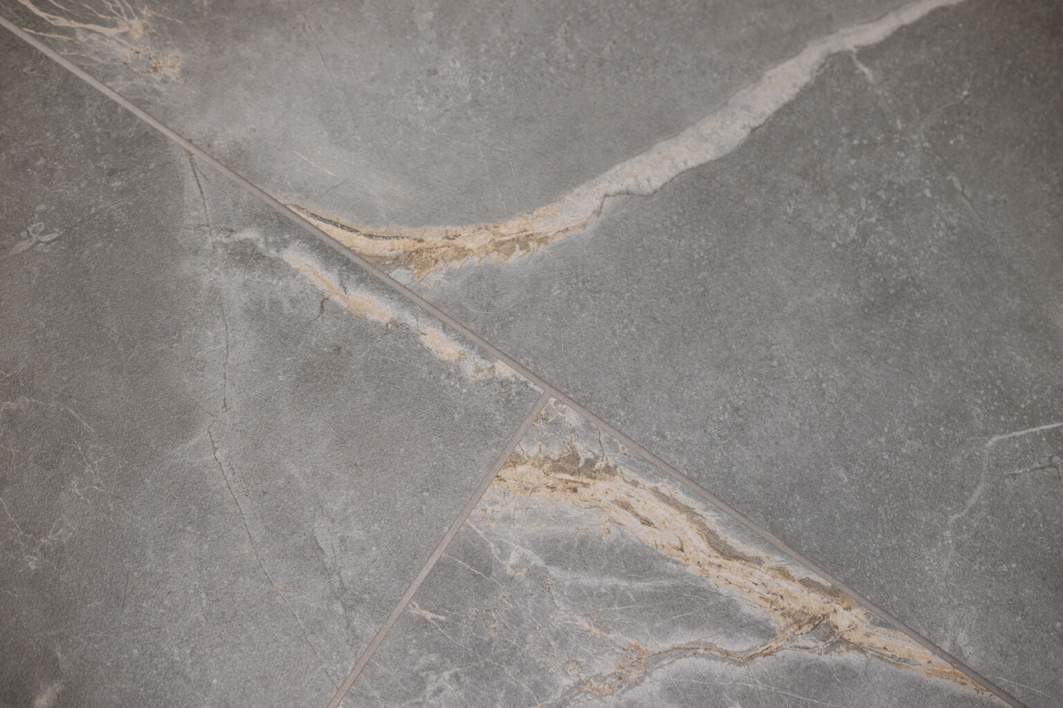 Close-up of grey stone tiles with diagonal beige and white veining patterns intersecting along the grout lines.
