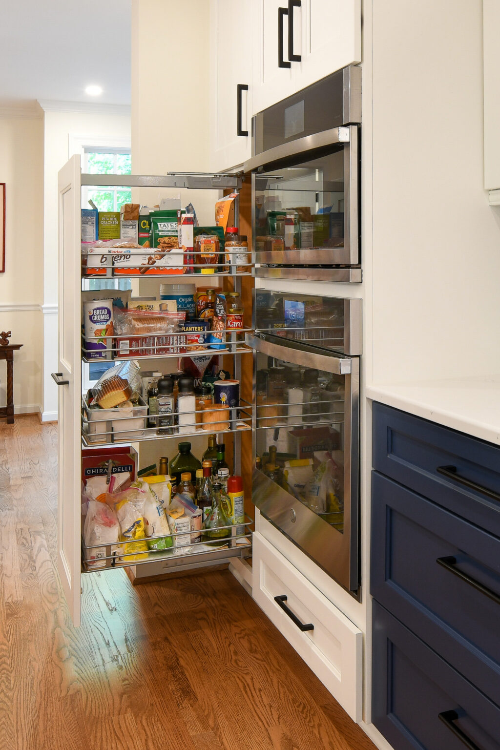 A well-organized pantry drawer is pulled open in a kitchen, revealing shelves stocked with food items, condiments, and snacks.