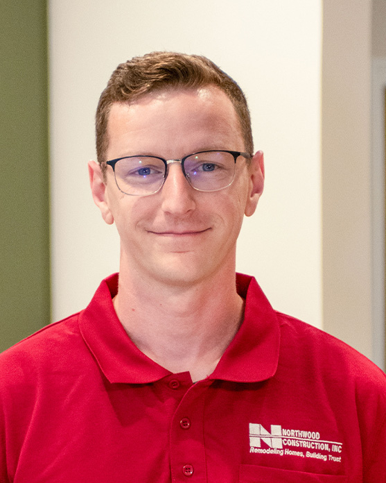 A man wearing glasses and a red polo shirt with a Northwood Construction, Inc. logo stands indoors, looking at the camera and smiling slightly.
