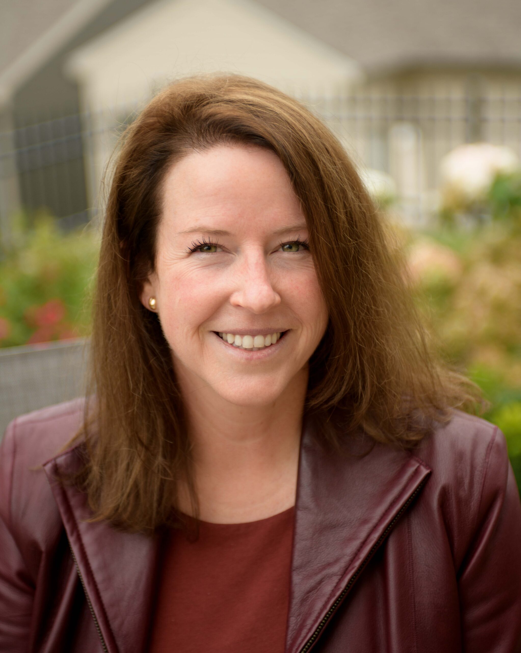 A smiling woman from our team with shoulder-length brown hair wearing a dark red jacket.