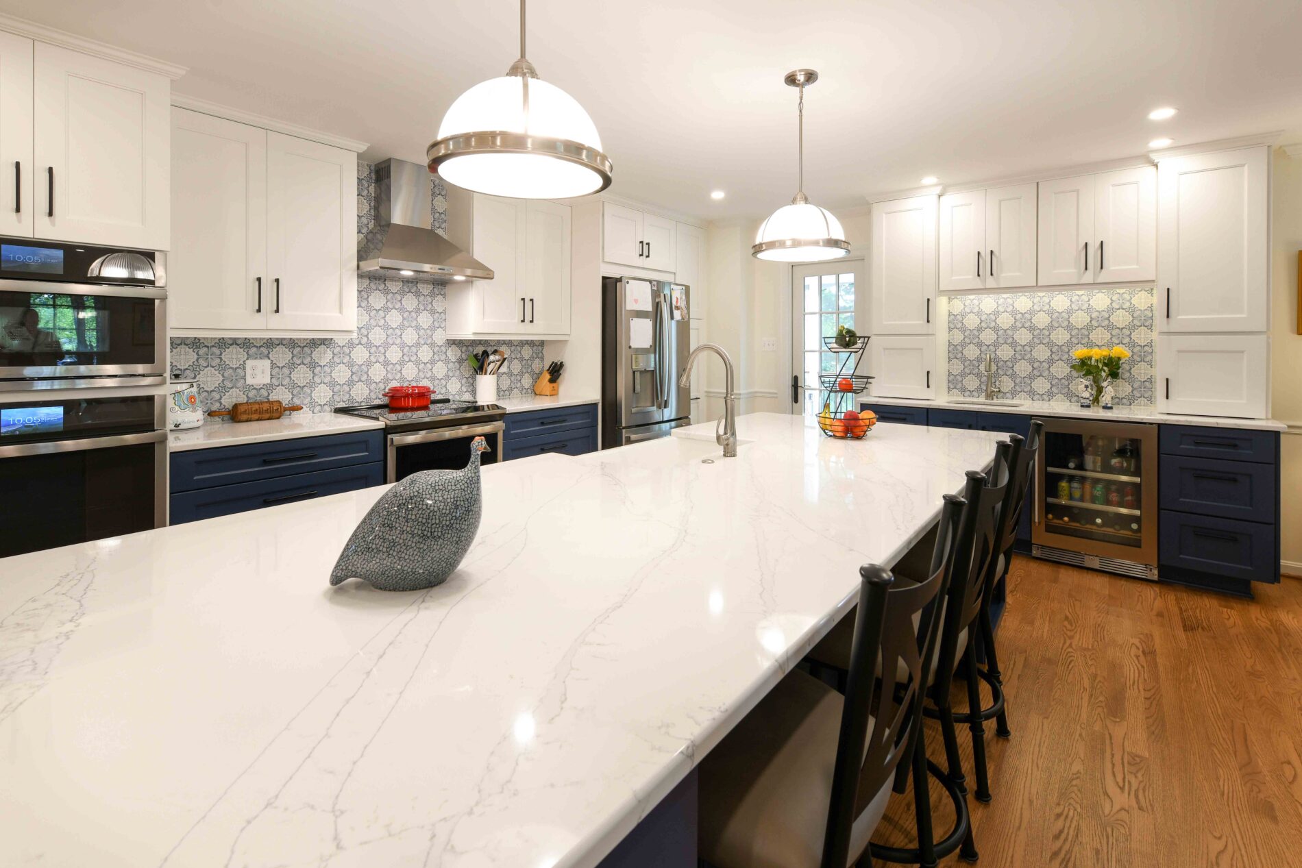 A kitchen with a large white quartz island, dark blue and white cabinetry, patterned tile backsplash, and two pendant lights.